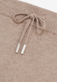 Beige Strickstoff-Jogginghosen mit einem breiten Rippenbund, Kordelzügen und silbernen Metall-Endstücken. Texturierte Oberfläche.