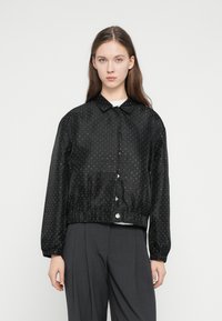 Čierna bunda s bodkami vyrobená z hladkej tkaniny; má golier, elastické manžety a zbieraný pás so zapínaním na gombík.