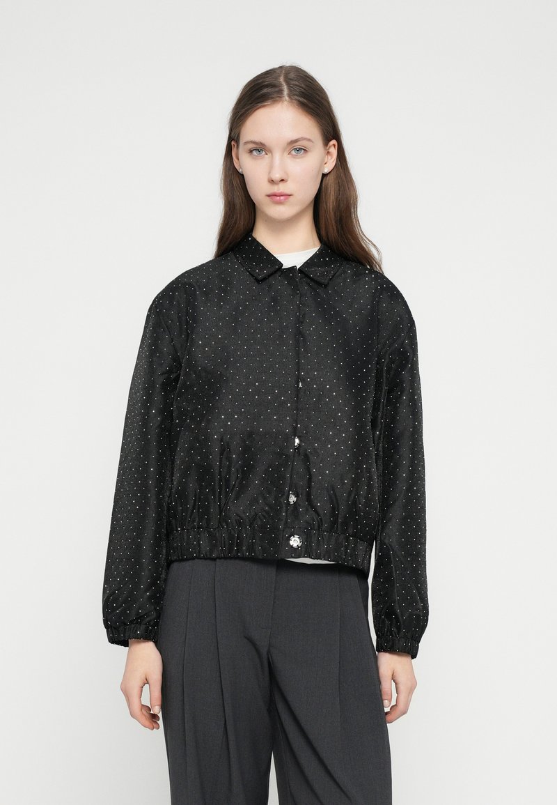 Čierna bunda s bodkami vyrobená z hladkej tkaniny; má golier, elastické manžety a zbieraný pás so zapínaním na gombík.