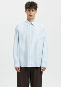 Lyseblå stripete skjorte i bomull med knapper, med en brystlomme foran og lange ermer med mansjettdetaljer, brukt sammen med mørke bukser.