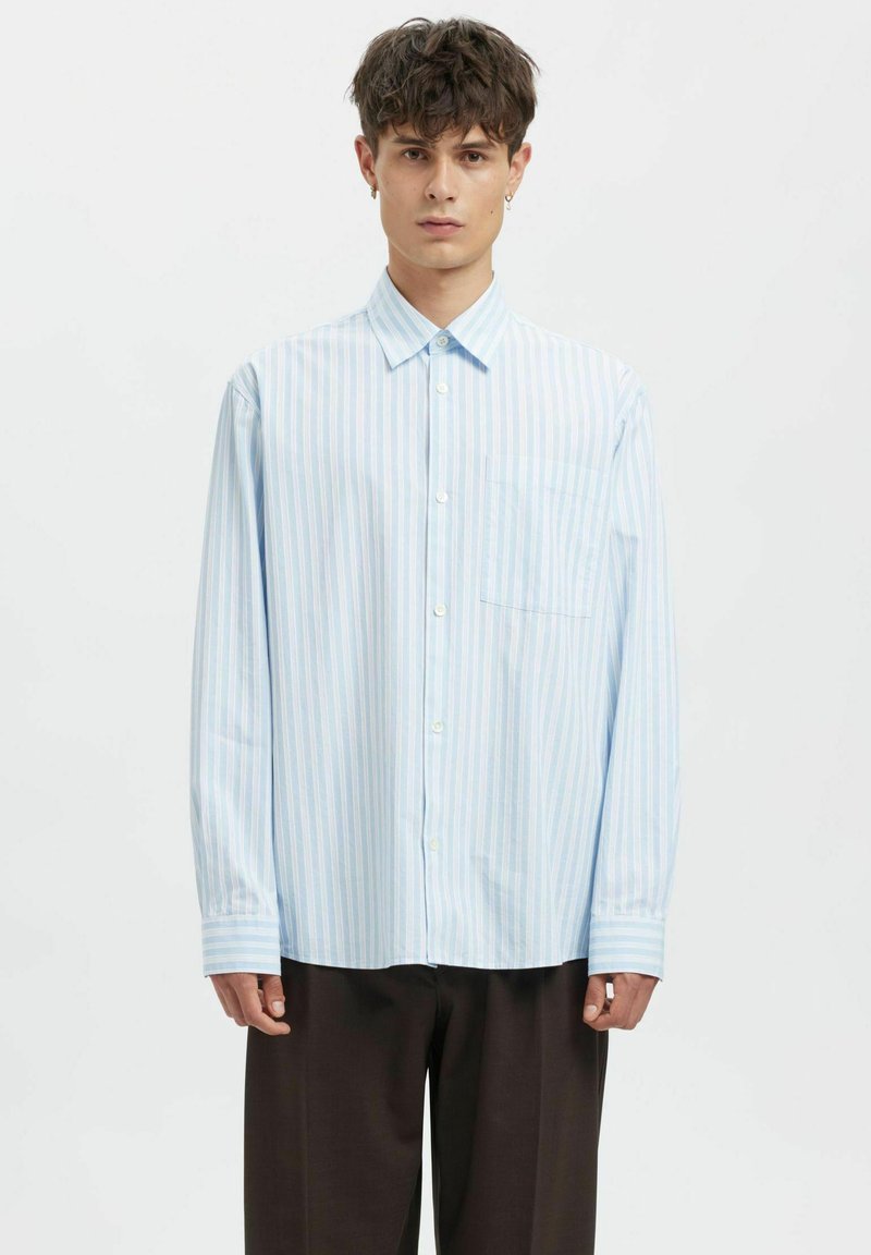 Lyseblå stripete skjorte i bomull med knapper, med en brystlomme foran og lange ermer med mansjettdetaljer, brukt sammen med mørke bukser.