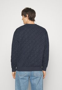 Felpa blu navy con texture trapuntata, caratterizzata da un motivo a logo diagonale. Maniche e orlo a coste, vestibilità comoda e scollo rotondo.