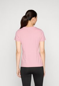 Šviesiai rožinė trumpa rankovė T-shirt, pagaminta iš minkštos medžiagos, su klasikinės apvalios iškirptės ir laisvu siluetu, derinama su juodomis prigludusiomis leggingais.