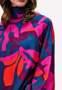 Blouse colorée avec un col montant, ornée d'un motif floral en rose, orange et bleu marine. Texture douce et coupe ample.