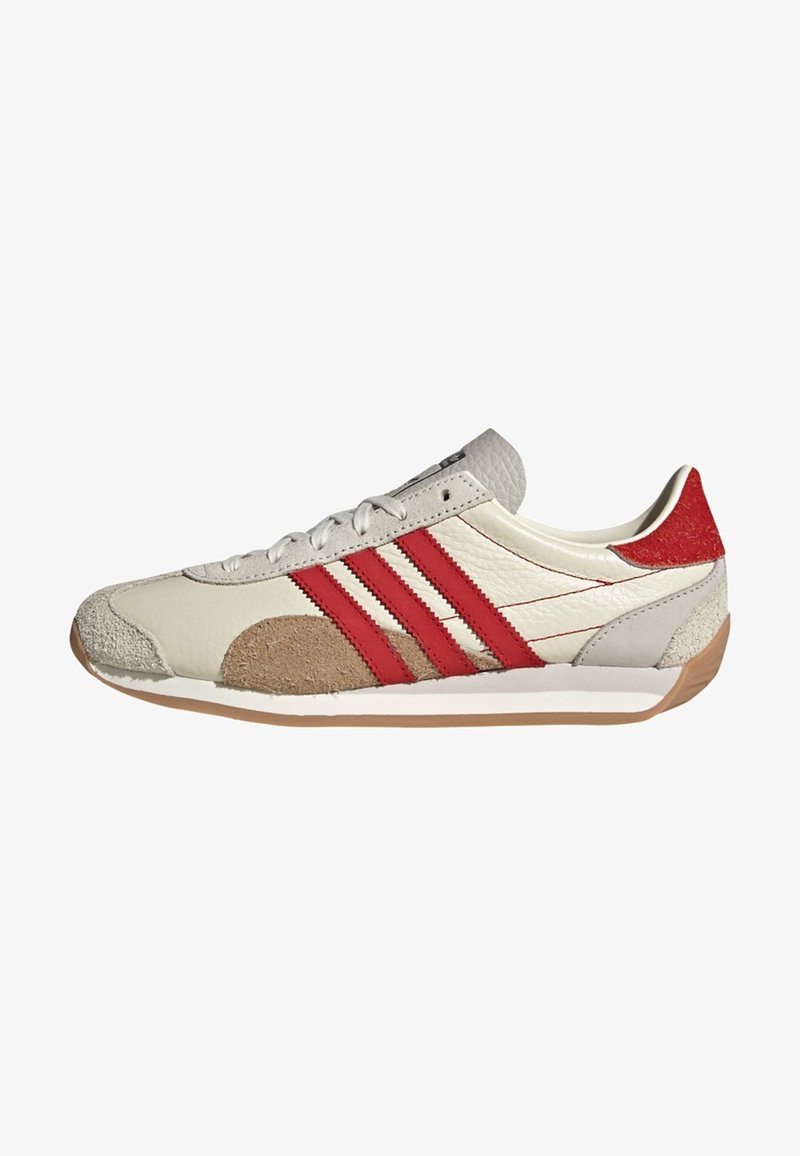 Fehér bőr sneaker három piros csíkkal, barna és piros velúr részletekkel, texturált részletekkel és gumi talppal.