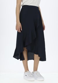 Marineblauwe maxi-rok met een asymmetrische gerimpelde zoom, gemaakt van een vloeiende stof. Gemaakt in combinatie met witte platform sneakers.