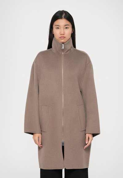Καφέ fleece παλτό με ψηλό γιακά, μπροστινό φερμουάρ και δύο μπροστινές τσέπες. Έχει χαλαρή εφαρμογή και μακριά μανίκια.