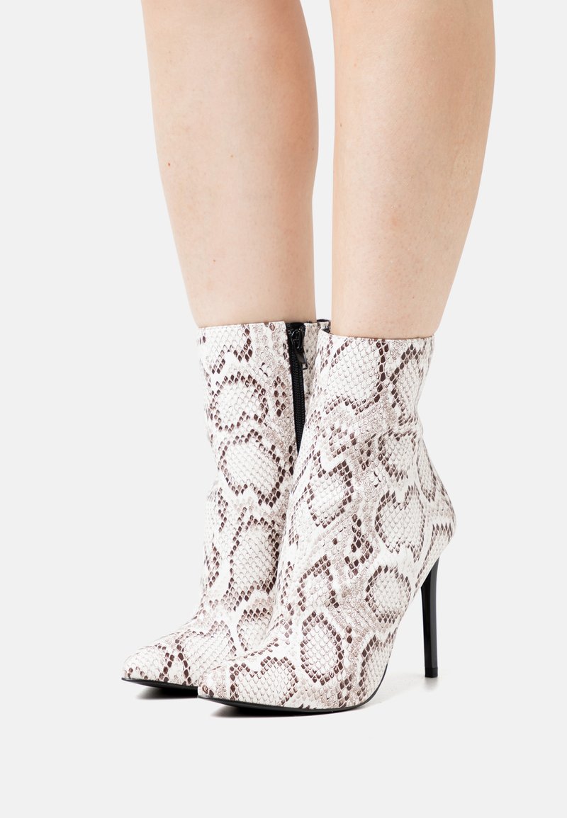 Botas de tornozelo de bico fino com padrão de pele de serpente, em branco e castanho, feitas de material texturizado, apresentando um fecho éclair preto e saltos agulha.