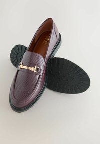 Burgundske kožne mokasine s teksturiranim završetkom, zlatnim kopčom i izdržljivim crnim gumiranim potplatom s uzorkom gaznoga sloja.
