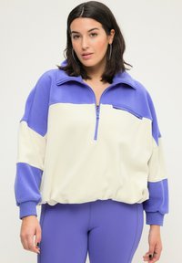 Fleece-Half-Zip-Pullover in hellem Creme und Lavendel, mit hohem Kragen, langen Ärmeln und einem cropped Schnitt mit gerippten Bündchen.