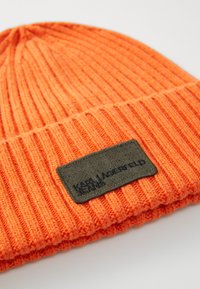 Orange knitted beanie with ribbed texture and a black rectangular label featuring embossed text. Designed for warmth and casual wear.