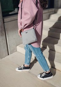 Šedá křížová taška s černými akcenty, nošená s růžovou oversized bundou a obnošenými modrými džíny, doplněná o černé tenisky.