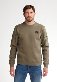 Sudadera verde oliva con textura acanalada, cuello redondo y parches de tela en contraste en los hombros. Presenta un pequeño logotipo en el pecho.