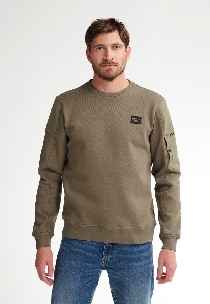 Sudadera verde oliva con textura acanalada, cuello redondo y parches de tela en contraste en los hombros. Presenta un pequeño logotipo en el pecho.