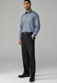 Camisa de manga larga azul claro, pantalones formales negros y zapatos negros. La camisa tiene un diseño elegante con cuello puntiagudo y silueta ajustada.