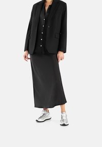 Blazer nero su una blusa in satin nera e una gonna midi nera, abbinato a scarpe sportive metallizzate argento.
