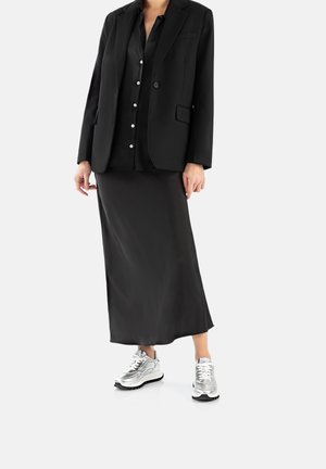 Blazer nero su una blusa in satin nera e una gonna midi nera, abbinato a scarpe sportive metallizzate argento.