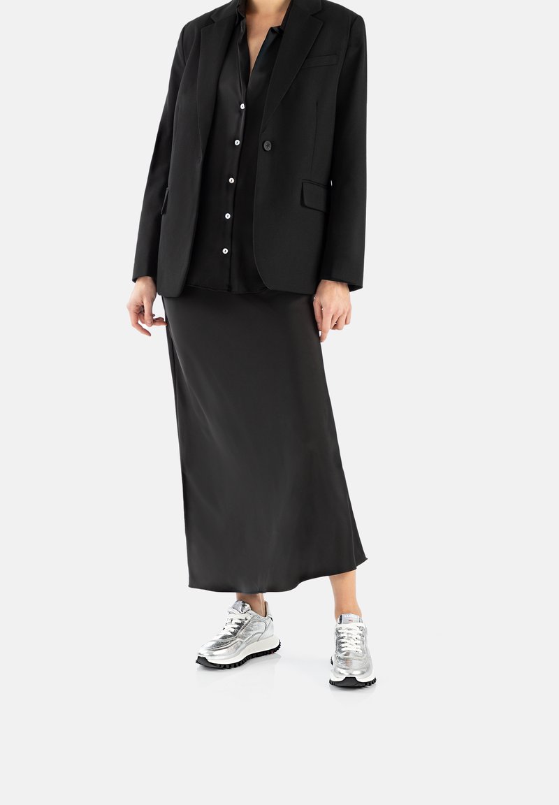 Blazer nero su una blusa in satin nera e una gonna midi nera, abbinato a scarpe sportive metallizzate argento.