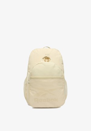 Zaino Reebok beige con tasca anteriore con cerniera, tasche laterali in rete, manico superiore e logo sul davanti su sfondo bianco.