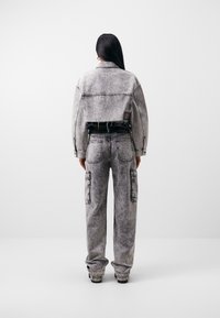 Harmaa farkkukangas cropped-takki ja siihen sopivat cargo-housut, joissa on haalistunut pinta, suuret taskut ja kontrastianiitti.