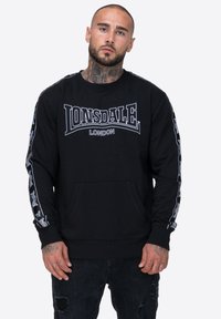 Czarna bluza z kapturem z dużym białym logo "LONSDALE LONDON" na klatce piersiowej oraz wzorowanymi akcentami na rękawach. Posiada kieszeń z przodu.