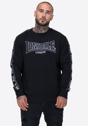 Czarna bluza z kapturem z dużym białym logo "LONSDALE LONDON" na klatce piersiowej oraz wzorowanymi akcentami na rękawach. Posiada kieszeń z przodu.
