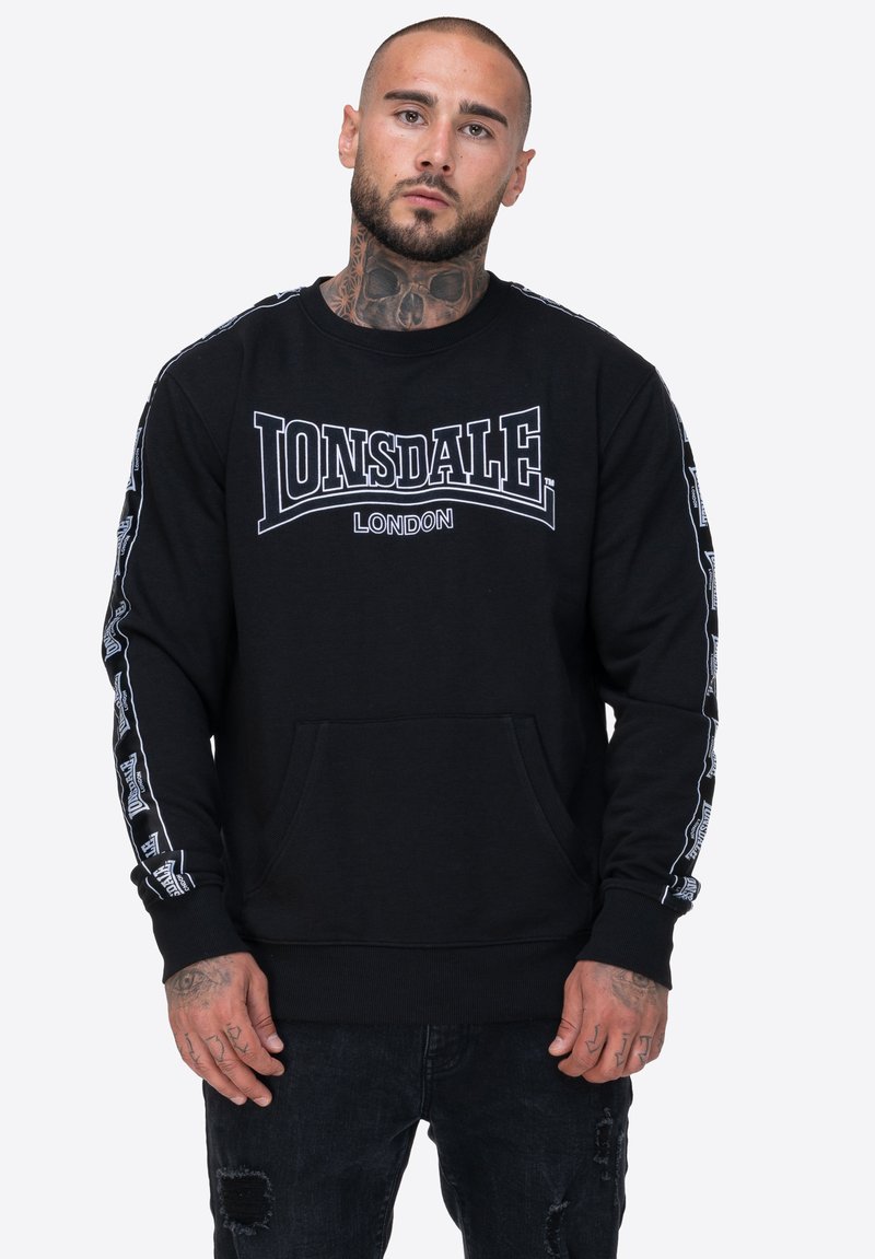 Czarna bluza z kapturem z dużym białym logo "LONSDALE LONDON" na klatce piersiowej oraz wzorowanymi akcentami na rękawach. Posiada kieszeń z przodu.