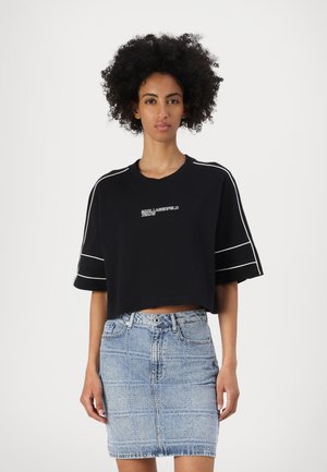 Black cropped t-shirt with white accents and logo, paired with a light blue denim skirt featuring a grid pattern and front buttons.