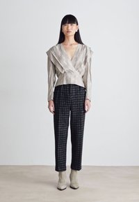 Top gri deschis, cu umeri unghiulari, combinat cu pantaloni în carouri alb-negru și cizme bej până la gleznă. Textură netedă și design structurat.