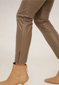 Ruskeat keinonahkapø pantsit, joissa on istuva muotoilu ja sivunappiyksityiskohta helmassa. Yhdistetty beigeihin nilkkasuksiin, joissa on vetskari.