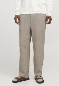 Pantalones beige a rayas con corte relajado, que presentan una textura suave y un diseño de pierna recta. Llevados con sandalias marrones.