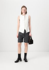 Hvit ermeløs topp med knappelukking, grå denimshorts, svarte ankelstøvler og en liten svart veske. Glatte teksturer og skreddersydd design.