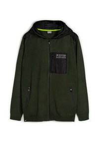 Veste à capuche zippée en tissu vert foncé avec des panneaux d'épaule noirs, une poche poitrine texturée et une doublure intérieure contrastante ; comporte des poches zippées à l'avant.