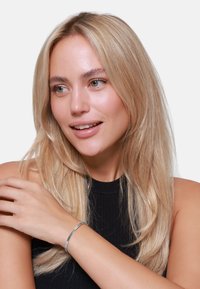 Bracciale in metallo argentato indossato a un polso, caratterizzato da un design elegante e minimalista. Il modello ha capelli lunghi e lisci ed indossa un top nero.