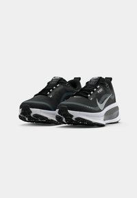 Een paar zwarte en grijze Nike hardloopschoenen met witte middenzolen, zwarte buitenzolen en reflecterende swoosh-logo's op een witte achtergrond.