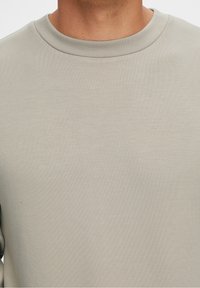 Sudadera gris claro de cuello redondo con tejido texturizado, que presenta un cuello de canalé y un acabado suave, diseñada para la comodidad y el uso casual.