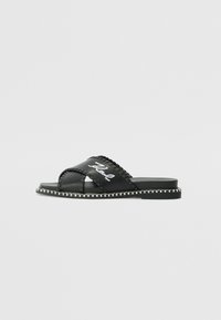 Black slide sandal with two wide straps, textured stitching, and white logo. Features a flat sole with contrasting decorative edge.
