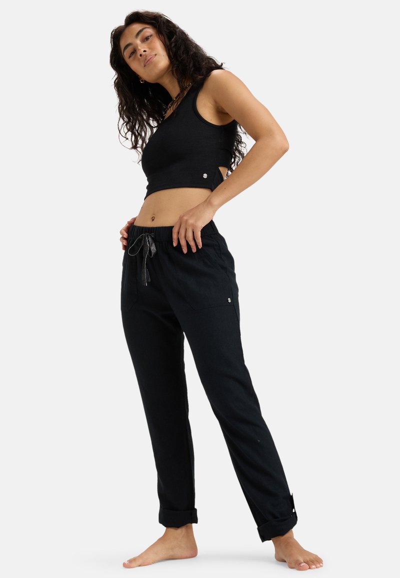 Black cropped tank top with side cutouts paired with black drawstring trousers featuring rolled cuffs and front pockets.