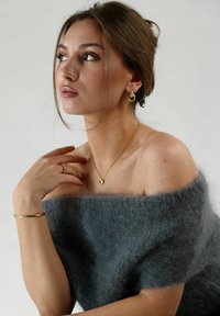 Suéter gris de lana suave y con los hombros al descubierto; collar de corazón dorado; pendientes de aro con acentos texturizados; anillos delicados y una pulsera que realzan el look.