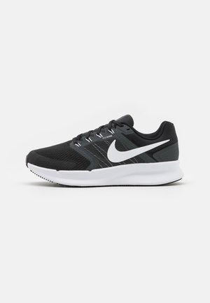 Zapatilla de running Nike en blanco y negro con parte superior de malla, sistema de cordones Flywire y suela blanca gruesa, mostrada de lado sobre un fondo liso.