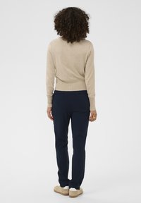 Beež pullover pikade varrukatega, kombineeritud tumesiniste pükstega. Riietus on kujundatud sobivalt, sisaldades minimaalset kujundust.