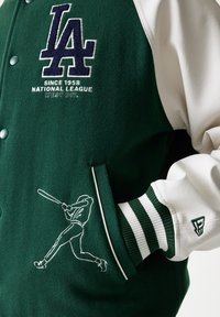 Πράσινο και λευκό τζάκετ varsity με μαλλινό κορμό, δερμάτινα μανίκια, λογότυπο LA, κέντημα αθλητικού στιλ και ριγέ μανσέτες. Περιλαμβάνει μπροστινές τσέπες.