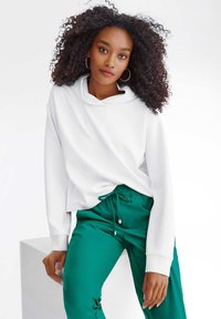 Witte hoodie met een ontspannen pasvorm en lange mouwen, gecombineerd met groene joggingbroek met een soepele textuur.