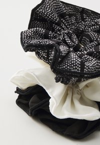 Twee stoffen haarbandjes, één zwart met witte stippen en één plain wit, met een zachte textuur en elastische banden voor haarstylings.