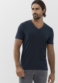 Námořnická modrá V-krková tričko z měkkého materiálu, krátké rukávy a přiléhavý střih. Nosič má na sobě šedé džíny. Hladká textura, minimalistický design.