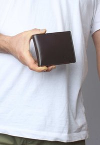 Brown leather wallet held in a hand, featuring a smooth surface, sharp edges, and subtle stitching details; no visible compartments.
