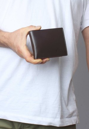 Brown leather wallet held in a hand, featuring a smooth surface, sharp edges, and subtle stitching details; no visible compartments.