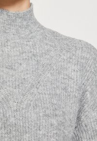 Pull en maille gris avec col haut, présentant un motif texturé et un design côtelé au niveau du cou et des épaules.