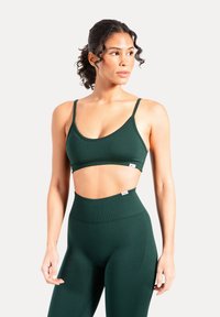 Ciemnozielony sportowy biustonosz z regulowanymi ramiączkami i gładkim, bezszwowym designem, zestawiony z dopasowanymi, wysokim stanem legginsami w podobnym kolorze.