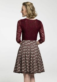Burgunderfarbene Spitzentop mit drei Viertelärmeln, kombiniert mit einem plissierten Blumenrock in den Farbtönen Bordeaux, Creme und Grün.